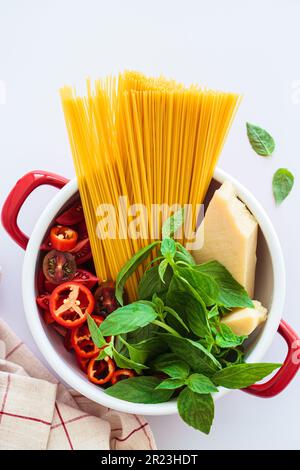 Ein Teigtopf. Rohe Zutaten für Pasta: Spaghetti, Parmesan, Gemüse und Basilikum in einem Kochtopf, Draufsicht. Stockfoto