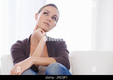 Ich Frage mich... Eine junge Frau, die auf ihrer Couch saß und aufmerksam aussah. Stockfoto