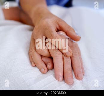 Sowohl in guten als auch in schlechten Zeiten. Nahaufnahme von Händen, die in Einheit und Komfort auf einem Krankenhausbett gefesselt sind. Stockfoto