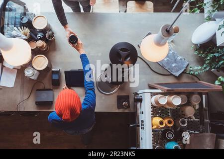 Der Verkäufer mit roter Mütze gibt einem Gast in einem Café Kaffee. Stockfoto