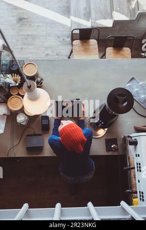 Der Verkäufer mit roter Mütze gibt einem Gast in einem Café Kaffee. Stockfoto