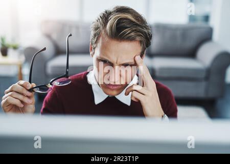 Hören Sie nicht auf, bis Sie eine Lösung gefunden haben. Ein junger Mann, der unter Stress leidet, während er einen Computer an seinem Schreibtisch benutzt. Stockfoto