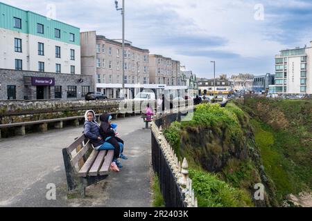 Leute, die sich auf Bänken mit Blick auf Tolcarne Beach an der Küste in Newquay in Cornwall in Großbritannien entspannen. Stockfoto