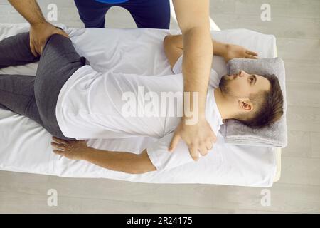 Der junge männliche Osteopath arbeitet an der Lendenwirbelsäule des jungen Patienten, um die Wirbel auszurichten. Stockfoto