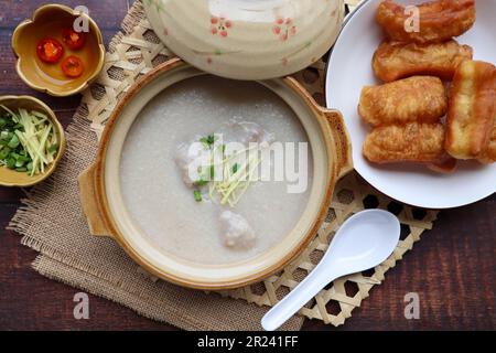 Congee mit Hackfleisch aus Schweinefleisch in Tontopf serviert mit frittierten Teigstäbchen von oben auf dem Holztisch - thailändisches Essen namens Jok Moo Stockfoto