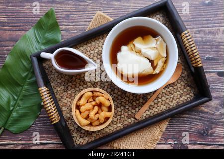 Douhua - weicher Tofu-Pudding (Sojabohnenquetsch), asiatisches berühmtes gesundes Dessert, serviert in Bambus-Tablett mit Holztisch von oben Stockfoto