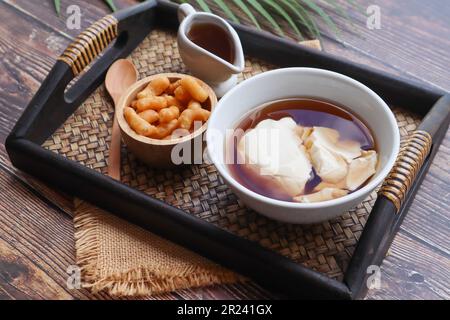 Douhua - weicher Tofu-Pudding (Sojabohnenquetsch), asiatisches berühmtes gesundes Dessert, serviert in Bambus-Tablett aus Holz bei Nahaufnahme Stockfoto