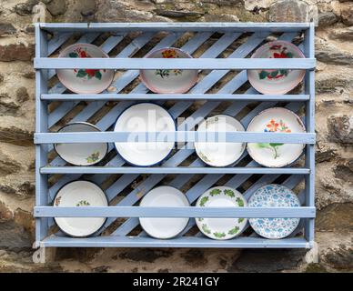 Alte Schimmel- und kunstvoll verzierte Emaille-Platten auf Holzregal Stockfoto