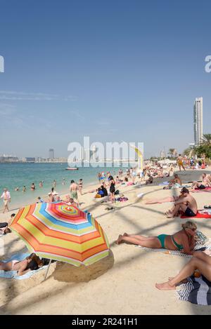 Sonnenanbeter und Wolkenkratzer am Marina Beach in Dubai, Dubai, Vereinigte Arabische Emirate Stockfoto