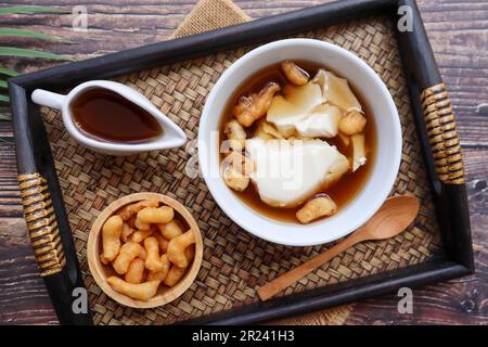 Douhua - weicher Tofu-Pudding (Sojabohnenquetsch), asiatisches berühmtes gesundes Dessert, serviert in Bambus-Tablett mit Holztisch von oben Stockfoto