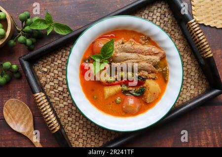 Rotes Curry mit gerösteter Ente: Thailändisches Essen namens Kang Pled Ped Yang mit Blick auf das Bambusblech auf dem Holztisch Stockfoto