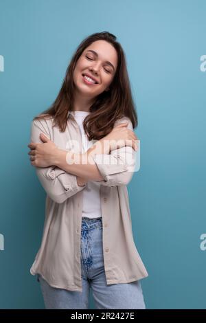 Romantische, träumende junge, brünette frau in Hemden und Jeans auf blauem Hintergrund Stockfoto