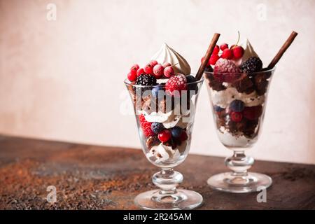 Schokoladenbrownies, frische Beeren, Baiser und Schlagsahne in Gläsern. Köstliches Dessert im Sommer. Stockfoto