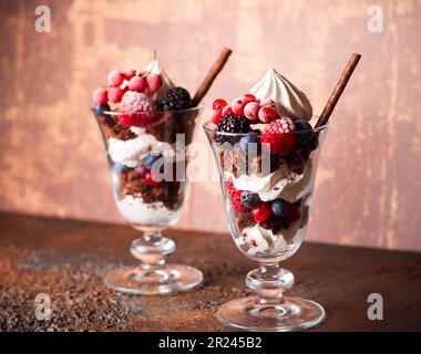 Schokoladenbrownies, frische Beeren, Baiser und Schlagsahne in Gläsern. Köstliches Dessert im Sommer. Stockfoto