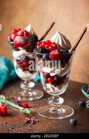 Schokoladenbrownies, frische Beeren, Baiser und Schlagsahne in Gläsern. Köstliches Dessert im Sommer. Stockfoto