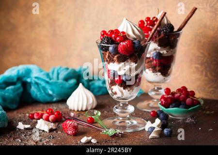 Schokoladenbrownies, frische Beeren, Baiser und Schlagsahne in Gläsern. Köstliches Dessert im Sommer. Stockfoto