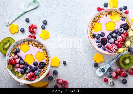 Smoothie in Schüsseln für ein gesundes Frühstück. Beerenjoghurt mit Heidelbeeren, Himbeeren, Brombeeren, roten Johannisbeeren, Mango, Kiwi und Bienenpollen Stockfoto