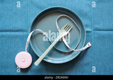 Leere marineblaue Keramikplatte mit Gabel und Maßband auf blauem Gewebetisch-Hintergrund. Konzept der gesunden Ernährung. Draufsicht Stockfoto