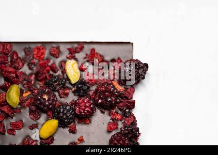 Draufsicht auf ein Schokoladenriegel mit getrockneten Erdbeeren, getrockneten Himbeeren und Pistazien auf weißem Hintergrund. Selektiver Fokus. Stockfoto