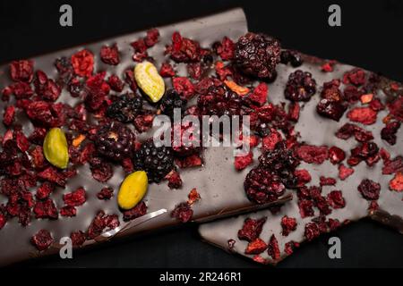 Schokoriegel mit Himbeeren, Erdbeeren und Pistazien auf schwarzem Hintergrund. Isoliert auf Schwarz. Selektiver Fokus. Stockfoto