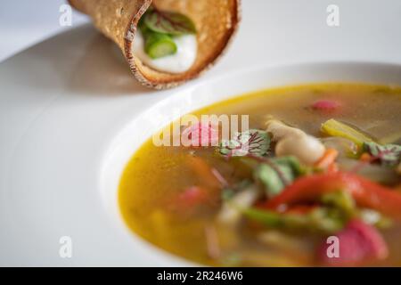Selektiver Fokus der Gemüsesuppe mit Spargel, Pilzen und rosa Gnocchi (Rote Bete) auf einer weißen Platte. Vegetarisches Essen. Stockfoto