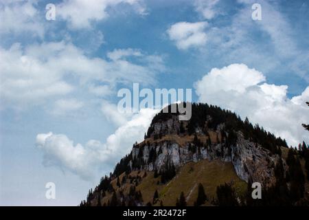 Natur's Palette: Eine malerische Berglandschaft erwacht in lebhaften Frühlingsfarben, während ruhige blaue Wolken die atemberaubende Szene anmutig einrahmen. Stockfoto