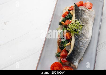 Gebackenes Seebarschfilet gefüllt mit Spinat, Pinienkernen und Kirschtomaten. Stockfoto