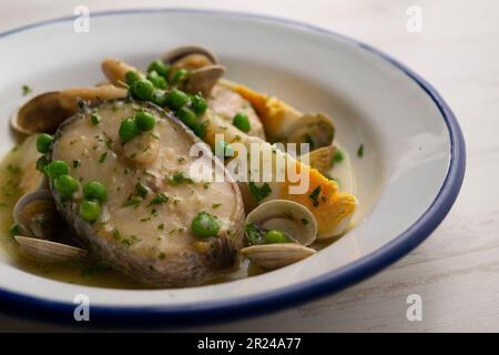 Baskischer Seehecht mit grüner Petersilie und Knoblauchsoße, serviert mit Spargel, Muscheln, hart gekochtem Ei und Erbsen. Stockfoto