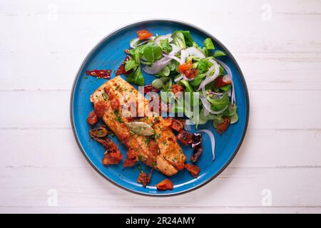 Pomfret gekocht mit Tomaten und serviert mit einem Salat auf einem blauen Teller. Stockfoto