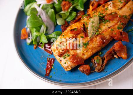 Pomfret gekocht mit Tomaten und serviert mit einem Salat auf einem blauen Teller. Stockfoto