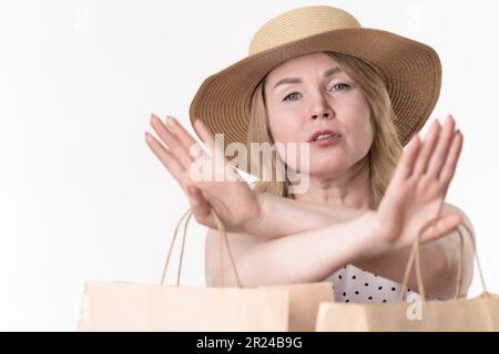 Eine seriöse Kundin streckte ihre gekreuzten Arme aus und zeigt ein Stoppschild. In den Händen einer Frau, die Handwerkstüten aus Papier hält, um einzukaufen Stockfoto