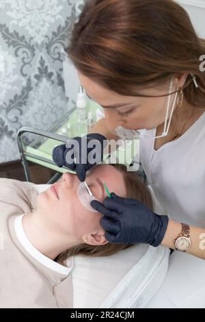 Kosmetikerin Reinigt Die Schlümpfe Der Jungen Frau Mit Augenpflastern Vor Der Laminierung Der Augenbrauen-Schönheitsbehandlung. Locken, Färben, Verlängerungsverfahren Für Stockfoto