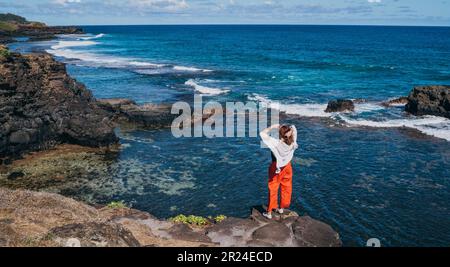 Einsame Frau kleidete leichte Sommerkleidung und genoss den Blick auf den Indischen Ozean mit starker Brandung auf den Klippen am Gris Gris Aussichtspunkt, extrem südlich der Insel Mauritius Stockfoto