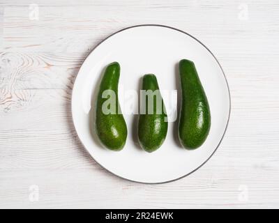 Drei Avocados auf weißem Teller auf Holzfläche Stockfoto