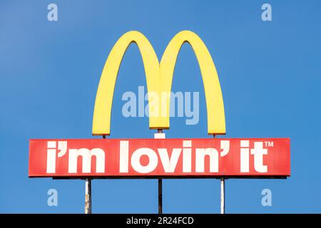 McDonalds Logo-Bogen-Schild und „I'm Lovin' IT“-Schriftzug gegen blauen Himmel mit Kopierbereich Stockfoto