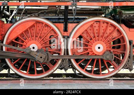 Große rote Räder, Schwungräder, Pleuelstangen und andere Maschinen einer alten Dampflokomotive. Stockfoto