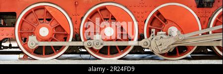 Große rote Räder, Schwungräder, Pleuelstangen und andere Maschinen einer alten Dampflokomotive. Stockfoto