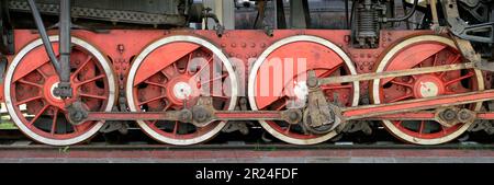 Große rote Räder, Schwungräder, Pleuelstangen und andere Maschinen einer alten Dampflokomotive. Stockfoto