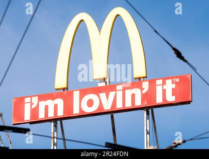 McDonald's Logo-Schild und „I'm Lovin' IT“-Schriftzug Unusual view, gesehen durch Überlandleitungen oder Straßenbahnkabel in städtischer Umgebung Stockfoto