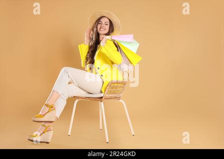 Glückliche Frau, die viele bunte Einkaufstaschen auf einem Sessel vor beigem Hintergrund hielt Stockfoto