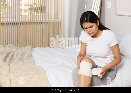 Junge Frau, die im Schlafzimmer einen Verband am Knie anlegt Stockfoto