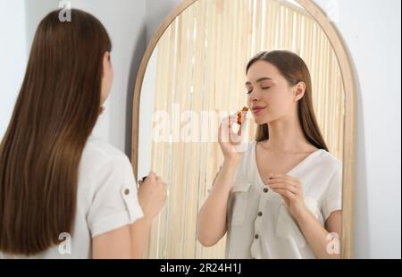 Junge Frau, die ätherisches Öl in der Nähe des Spiegels riecht Stockfoto