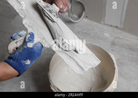 Professioneller Arbeiter, der im Innenbereich Putz auf Spachtelmesser legt, Nahaufnahme Stockfoto