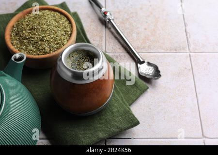 Calabash, Bombilla, Schüssel mit Teeblättern und Teekanne auf einem gefliesten Tisch, Platz für Text Stockfoto