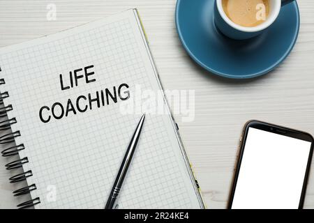 Satz Life Coaching in Notizbuch, Stift, Smartphone und Tasse Kaffee auf weißem Holztisch, flach liegend Stockfoto