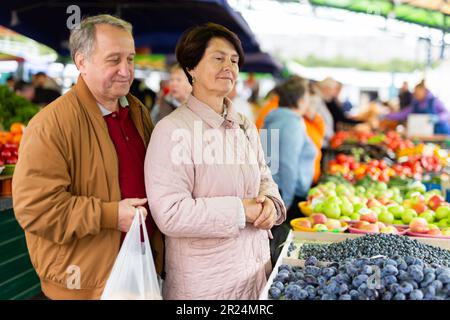 Glückliches, reifes Paar, das frische Blaubeeren pflückt, während wir zusammen auf dem lokalen Markt einkaufen Stockfoto