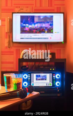 Zwei schwarze Mikrofone zum Singen von Liedern auf einer Tischecke neben zwei Getränkegläsern in einem japanischen Karaoke-Club-Raum mit einem Controller, der von hinten beleuchtet ist Stockfoto