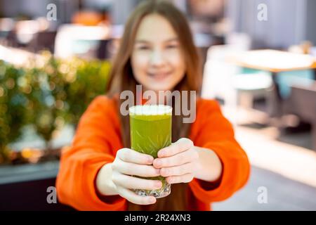 Glückliche Mädchen halten und trinken grüne gesunde Ernährung nahrhaften Cocktail. Konzentrieren Sie sich mit Glas im Freien auf Ihre Hände Stockfoto