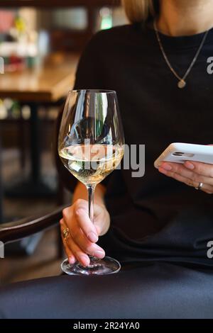 Ein Glas Weißwein in den Händen eines Mädchens, das sich in einem Restaurant entspannt. Verkostung alkoholischer Getränke. Sommerruhe. Romantischer Aperitif am Abend Stockfoto