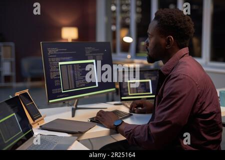 Junger afroamerikanischer Programmierer, der sich auf die Arbeit mit Codes konzentriert, während er am Tisch sitzt und am Computer arbeitet Stockfoto